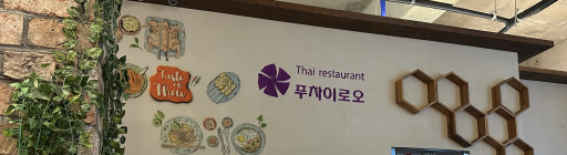 카운터 위 벽 — 보라색 바람개비 표지와 "Thai restaurant 푸차이로오", 음식 그림, "Taste of Thai" 판, 육각 나무 선반